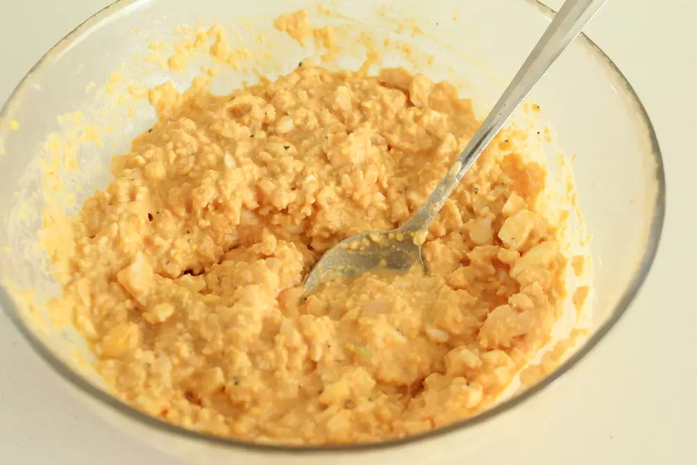 使い捨ての手袋をして、手でゆで卵を潰し、みじん切りにした玉ねぎを加える。調味料も加えてスプーンでしっかり混ぜる。